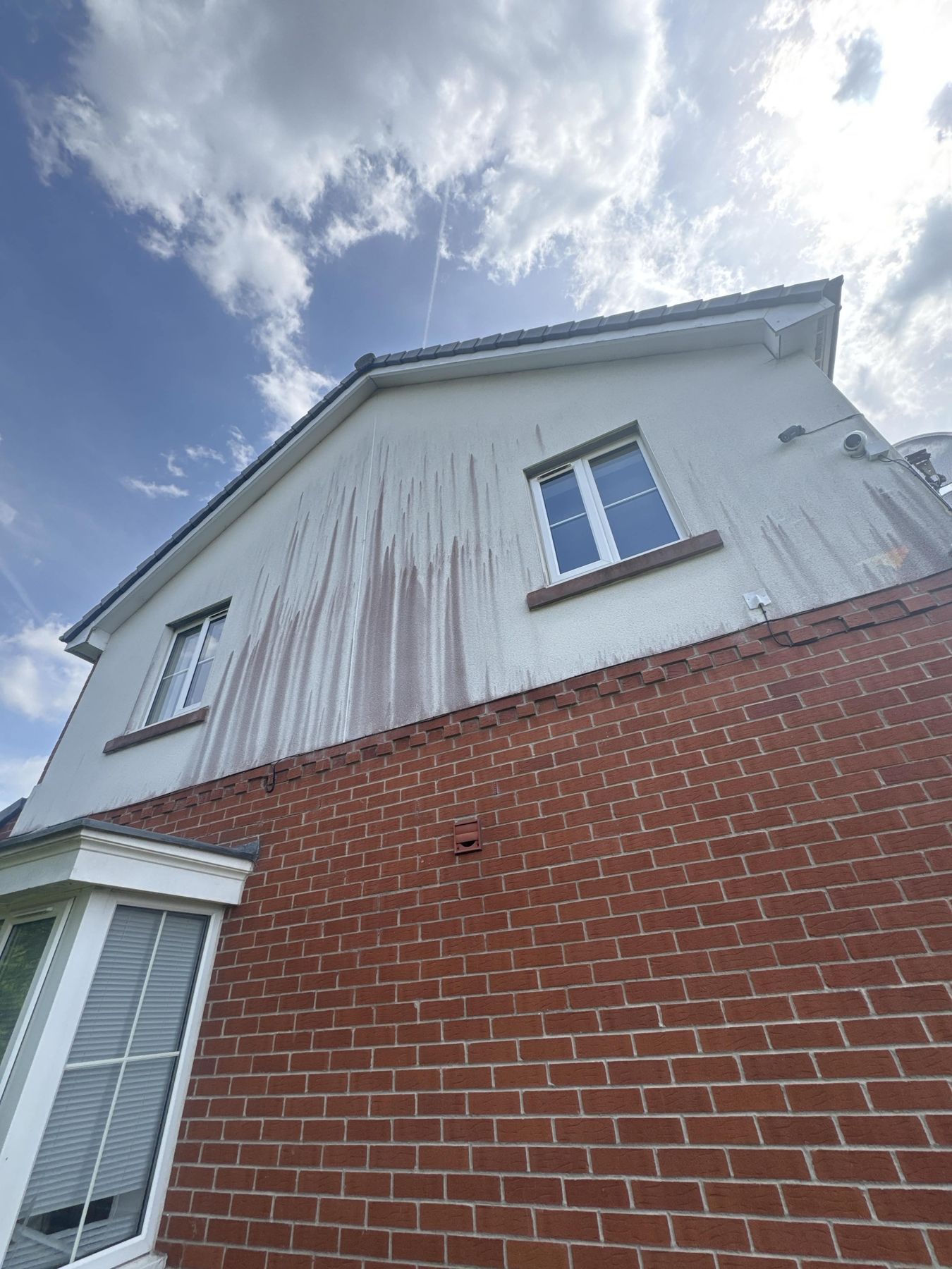 Gable end render before cleaning — brown and rust coloured streaks running down white render